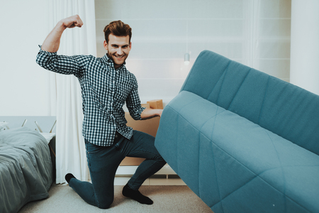 The guy moves the sofa while moving to a new home. The guy does a reshuffle in the room.の写真素材