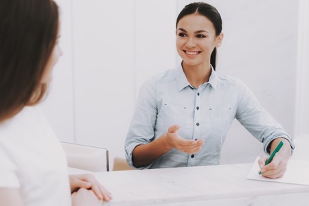 Woman Receptionist. Reception Workplace. Workplace in Beauty Salon. White Interior. White Reception Desk. Beauty Consept. Smiling Salon Employee. Customer Registration. Employee Talking Client.の写真素材