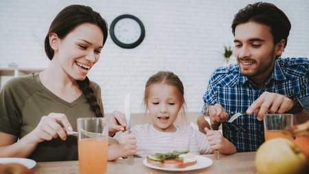 Family Breakfast. Parents Looking Sandwich. Breakfast for Happy Family. Fruit on Plate. Bread on Plate. White plate. Juice in Glass. Food on Table. Happy Family. Smiling People. Vegetarian Food.の写真素材
