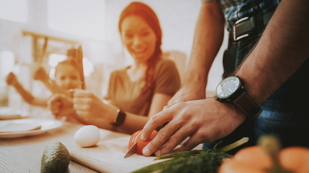 Man Cooking. Family Breakfast. Breakfast Happy Family. Fruit on Plate. Bread on Plate. White plate. Slicing Vegetables. Vegetables on Board. White Interior. Man with Clock. Tomato and Cucumber.の写真素材