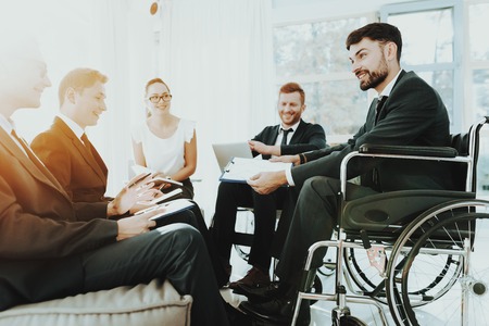 Person in Wheelchair. Group Disabled Worker. Panoramic View. White Interior. People with Limited Opportunities. Business Meeting. Business Clothes. Business Suits. Work Process. Man in Wheelchair.の写真素材