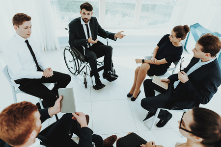 Person in Wheelchair. Healthy Person and Disabled. Panoramic View. Bright Interior. People with Limited Opportunities. Business Meeting. Business Clothes. Discuss Concept Work. Man in Wheelchair.の写真素材
