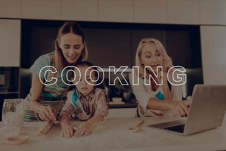 Together at Home. Laptop. Girl Knead Dough. Home-Made. Preparing Cake. Rolling Pin. Aprons. Woman. Grandmother. Have Fan. Recipes. Smile. Thanksgiving Day. Happy Family. Kitchen. Celebrating Holiday.の写真素材