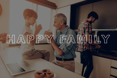 Drinking Tea. Laptop. Washes Dishes. Vegetables. Tomatoes. Countertop. Happy Family. Dinner. Boy. Together at Home. Father. Thanksgiving Day. Fan. Celebrating Holiday. Kitchen. Traditional Dinner.の写真素材