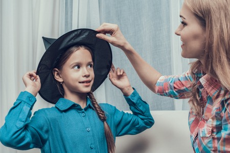 Beautiful Woman putting Witch Hat on Little Girl. Young Mother helping Cute Smiling Daughter with Costume for Halloween Party. Celebration of Halloween. Family and Childhood Conceptの写真素材