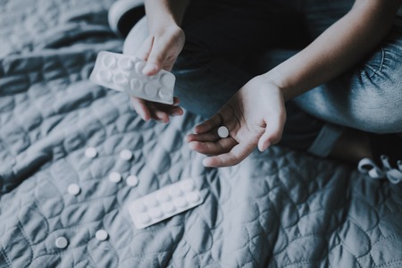 Closeup of Child Hands Holds Pills Sits on Bed with Crossed Legs.