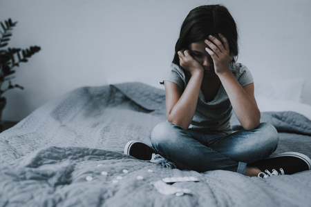 Little Girl Sits on Bed with Scattered Pills.の写真素材