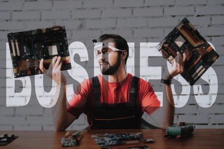 Tired Worker is Fixing Motherboard. Computer Service Employee is Depressed. Concept of Exhausting Job. Man Holding Two Broken Boards. Man Does Hard Work. Lot of Work at Technician Maintenance Center.の写真素材