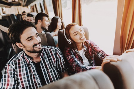 Young Smiling Couple Traveling on Tourist Bus. Handsome Man and Beautiful Woman in Headphones Relaxing on Passenger Seats of Tour Bus. Traveling, Tourism and People Concept. Happy Travelers on Tripの写真素材
