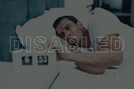 Disabled Man. Man is Lying in Bed. Man Woke Up. Clock on Table near Bed. 6:53 Time on Clock. Man Dissatisfied. Man is Not Sleepy. Adult Brunette Man. Man Located in Modern Bedroom.の写真素材