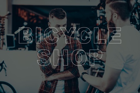 Bicycle Shop. Salesman Showing the Water Bottle to Customer. Water Bottle for Bicycle. Customer Choosing the Water Bottle. Hipster Male Salesman. Customer Thinking. Man Sales the Bicycles Equipment.