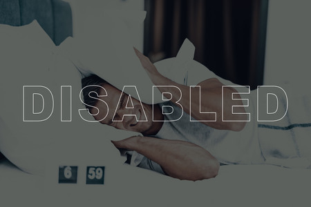 Disabled Man. Man is Lying in Bed. Man Woke Up. Clock on Table near Bed. 6:59 Time on Clock. Man is Angry. Man is Not Sleepy. Adult Caucasian Brunette Man. Man Located in Modern Bedroom.の写真素材