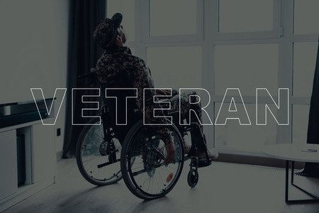 Military Veteran. Disabled Man in a Wheelchair. Man Sits in Front of Window. Man Looking Up. Man Thinking. Man is Soldier. Soldier in Military Uniform. Man Located in the Living Room.の写真素材