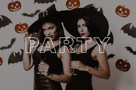 Wall with Black Bats. Lady on Halloween Party. Women with Glasses of Wine Smile. Women in Black Dresses. Girls in Witch Hats. Party in Magic Studio. Pretty Girls in Halloween Makeup. Gothic Look.の写真素材