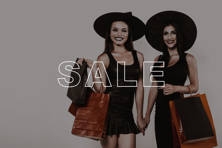 Lady on Sale in Shop Space. Two Women Broad Smile. Woman Visit Halloween Party. Girls in Black Dresses. Friends in Witch Hats. Pretty Friends Together in Shopping. Girls with Packages in Hands.の写真素材