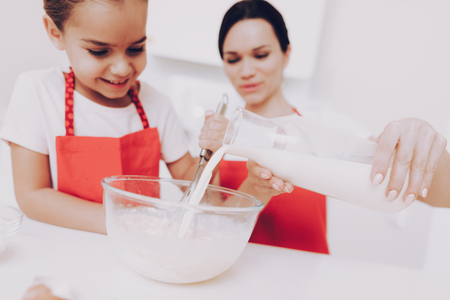 Milk for Cake. Beautiful Mother Help Yong Girl with Cake. Pours Milk in Dishes and Mix. Smile Girl and Happy Mother Cook Cake Together. Joi Young Girl with Mother Cooking. Young Mother Bake a Cake.の写真素材