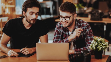 Freelance Photographers Review Photos on Laptop. Two Young Guys Discussing While Working on Laptop Looking at Camera Screen Working in Studio Office. Freelancers Teamwork and Cooperation Conceptの写真素材