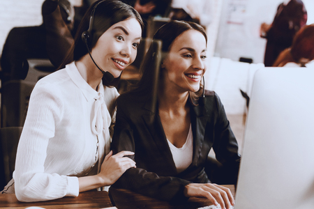 Two Young Smiling Women Working in Call Center. Manager with Computer. Girl on Workplace. Consultant with Microphone. Customer Service Concept. Operator in Office. Smiling Woman in Office.の写真素材