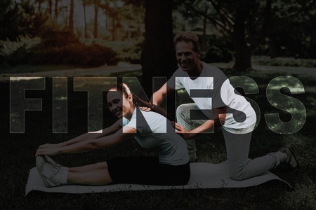 Young Fitness Woman. Man Helping Girl Stretch. Girl Doing Stretching on Rug. Yoga in Park. Girl in Fitness Training. Female Do Exercises in Park. Person Leads Healthy Lifestyle. Woman Smiles.の写真素材