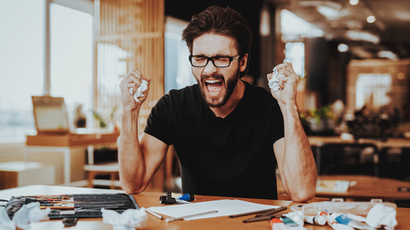 Stressed Guy Fails while Painting Indoors. Portrait of Handsome Nervous Caucasian Painter Using Color Paints Sitting at Table With Art Tools. Art Job and Artist Inspiration Problems Conceptの写真素材
