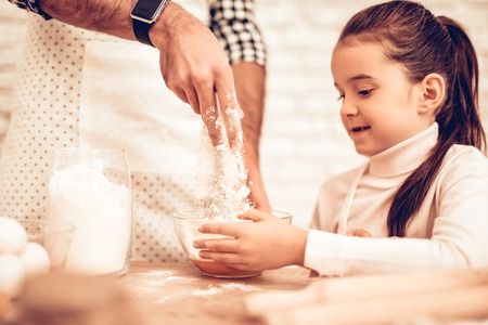 Cook Food at Home. Happy Family. Father's Day. Girl and Man Cooking Smiling Man and Child at Table. Spend Time Together. Food on Table. Break Egg in Bowl. Pour Flour. Cook Dough. Pour Flour in Bowl.の写真素材
