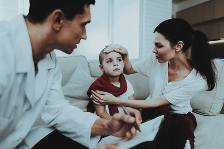 Doctor Visiting Little Girl in Red Scarf with Cold. Sick Young Girl. White Sofa in Room. Doctor in Uniform. Disease Concept. Healthcare and Healthy Lifestyle Concept. Mother with Daughter.の写真素材