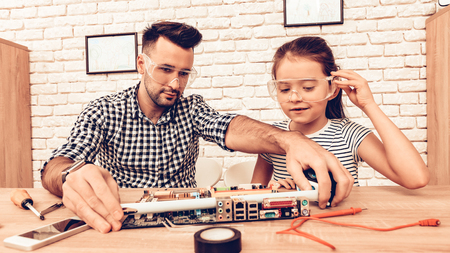 Man and Girl with Tool. Father and Daughter on Sofa. Spend Time Together. Father's day. White Interior. Review Device. Spare Parts on Table. Measure with Tape. Father Master and Daughter in Glasses.の写真素材