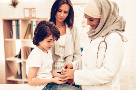 Arabic Doctor Measuring Blood Sugar Level Boy. Child at the Pediatrician. Hospital Concept. Healthy Concept. Child Patient Visiting Doctor. Doctor Checking Blood Sugar Level. ill Boy Lying on Bed near Mom. Diabetes.の写真素材