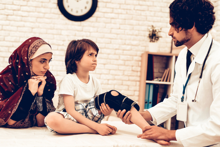 Arabic Male Doctor Bandaging Leg Injury of Child. Hospital Concept. Healthy Concept. Child Patient Visiting Doctor. Doctor Bandaging Leg Little Patien. Child Patient Visiting Doctor. Leg Injuryの写真素材