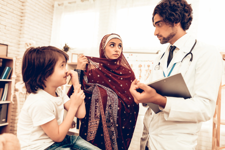 Arabic Pediatrician Appointment Mom with Sick Son. Confident Muslim Male Doctor. Hospital Concept. Healthy Concept. Pediatrician Writes a Prescription. Child Patient Visiting Doctor.の写真素材