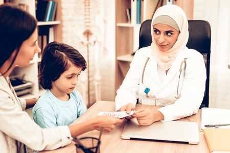 Smiling Patient Giving Money to Arabic Doctor. Confident Muslim Female Doctor. Child at the Pediatrician. Hospital Concept. Healthy Concept. Child Patient Visiting Doctor.の写真素材