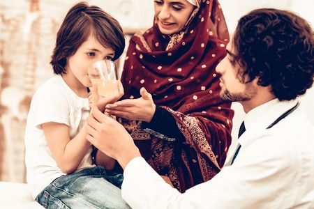 Arabic Male Doctor Give Medicine to Sick Boy. Confident Muslim Male Doctor Giving Glass of Medicine. Child at the Pediatrician. Hospital Concept. Healthy Concept. Child Patient Visiting Doctor.の写真素材