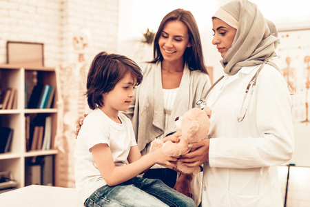 Arabic Doctor Giving Toy to Little Cute Patient. Confident Muslim Female Doctor. Child at the Pediatrician. Hospital Concept. Healthy Concept. Child Patient Visiting Doctor. Healthcare And Medicine.の写真素材