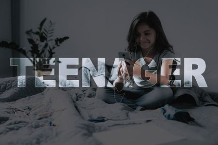 Child Listen Favorite Music. Girl Sit on Gray Bed. Girl Hold Smartphone and Headphones. Time Go to School. Child Get Up. Little Black-Haired Girl. Wonderful Morning. Smiling Girl. Student Weekdays.の写真素材