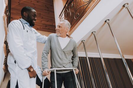 Man Holds On Walker for Adults. Old Bones Hard Walk Alone. Pensioner on Go-Carts. Caregiver Supports Man. Nursing Home.の写真素材