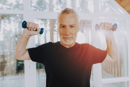 Active Retiree Wearing Sport Uniform. Smiling Patient Do Exercises. Elderly Hold Dumbbells. Therapeutic Gymnastics in Nursing Home. Man Looks Confident in Abilities.の写真素材