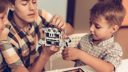 Teenager Demonstrating Robot to Two Sitting Boys. Young Boy in Shirt. Indoor Joy. Modern Hobby...