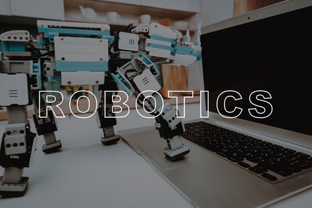 Close Up. Robot Stand on Kitchen Table. Robot Put Foot on Gray Laptop. Digital Computer. Mechanical Robotics. Innovation Technology. Technical Progress. Artificial Intelligence. Modern Technology.の写真素材
