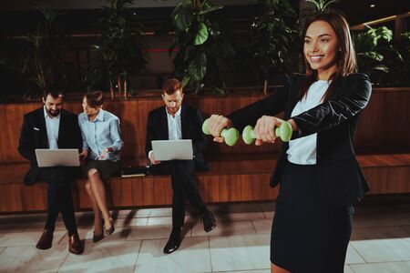 Sport Lifestyle. Healthcare of Business People. Yoga Practice. Girl Smiling. Training with Dumbbells in Workplace .Happy Young Woman. . Healthy Body. Success Worker Training. Sports Staffの写真素材