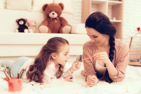 Fun with Daughter. Kids Home Games. Drawing with Pencils. Child Development. Mom and Daughter Play. Happy Mom and Child in Pajamas. Girl and Mother Lie on Carpet. Colour Pencils. Mom and Daughter Drawの写真素材