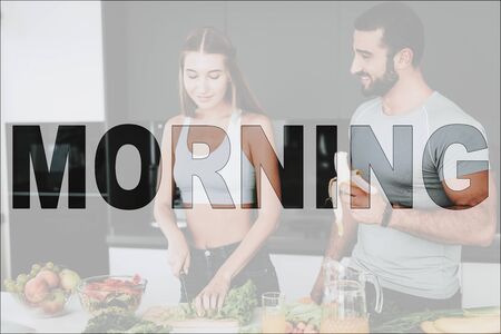 Happy Morning. Athletic Couple in the Kitchen. Vegetables and Fruits on Table. Couple Prepare a Salad. Woman Cutting a Salad on Wooden Board. Man Eating a Banana. Couple Have a Healthy Lifestyle.の写真素材