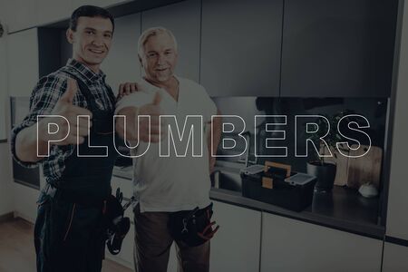 Two Male Plumbers. Plumbers is Adult Guy and Old Man. Workers Located in a Modern Kitchen. Men Wearing in a Special Uniform.の写真素材