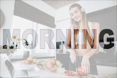 Happy Morning. Girl in Kitchen. Vegetables and Fruits on Table. Laptop on Table. Girl Prepare a Salad. Girl Cutting a Pepper.の写真素材