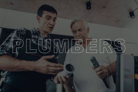 Two Male Plumbers are Working. Plumbers is Adult Guy and Old Man. Workers Located in a Modern Kitchen. Men Wearing in a Special Uniform.の写真素材