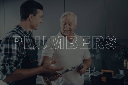 Two Male Plumbers are Working. Plumbers is Adult Guy and Old Man. Workers Located in a Modern Kitchen.の写真素材