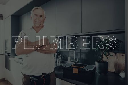 Old Gray Haired Man Posing. Man is Plumber. Plumber is Smiling. Tool Box on Table. Person with Arms Crossed.の写真素材