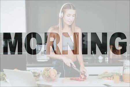 Happy Morning. Girl in Kitchen. Vegetables and Fruits on Table. Laptop on Table. Girl Prepare a Salad. Girl Cutting a Pepper. Girl Listening Music on Headphones. Girl Have a Healthy Lifestyle.の写真素材