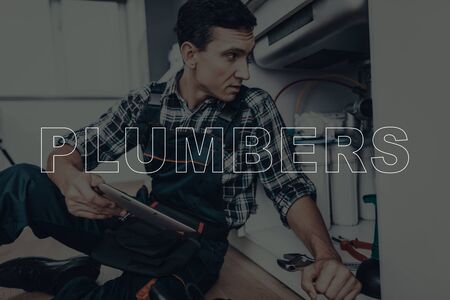 Adult Man are Working. Man is Plumber. Plumber Wearing a Special Uniform. Person in a Modern Kitchen Sitting on Floor.の写真素材