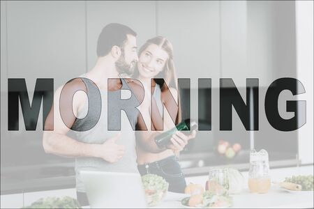 Happy Morning. Happy Couple in Kitchen. Vegetables and Fruits on Table. Laptop on Table. Man Holding a Vegetable Cocktail. Man Showing OK Sign. Girl Hugging a Man. Couple Have a Healthy Lifestyle.の写真素材