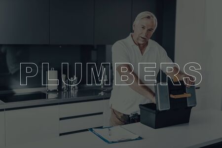Old Gray Haired Man Posing. Man is Plumber. Worker is Taking Tool from Tool Box. Tool Box on Table. Plumber Wearing White T-Shirt.の写真素材